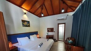 Hotelkamer met een houten plafond, een bed met witte lakens, een bureau met stoel en een raam met gordijnen.