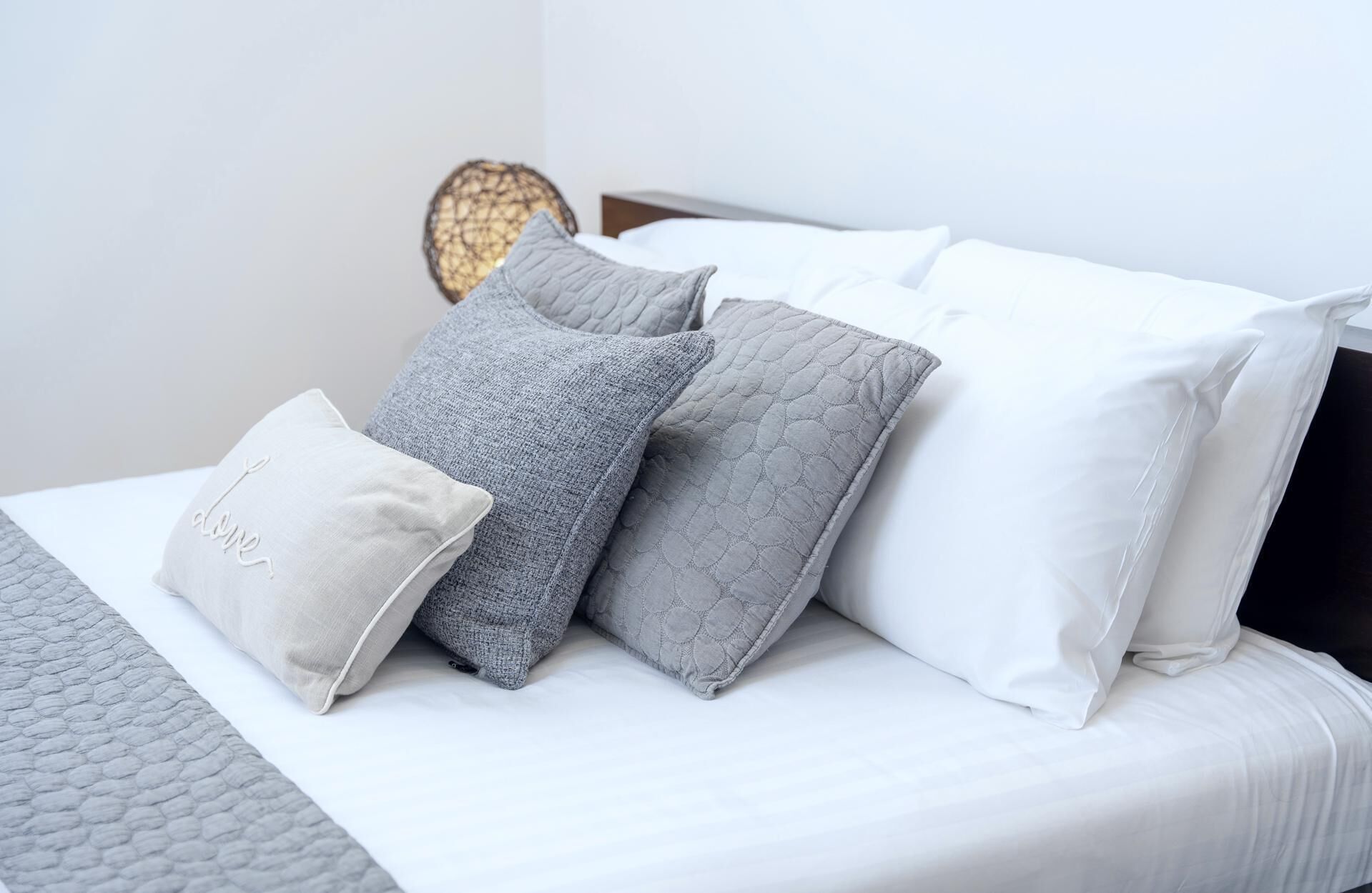 A neatly made bed with white and gray pillows, a textured gray blanket, and a decorative wall piece.