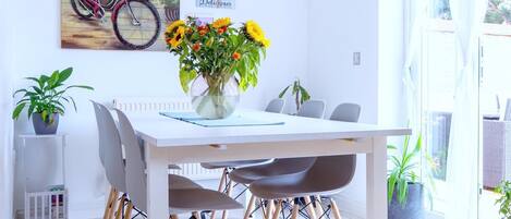 A modern dining area with a white table and chairs, a vase of sunflowers, and a bicycle painting on the wall.