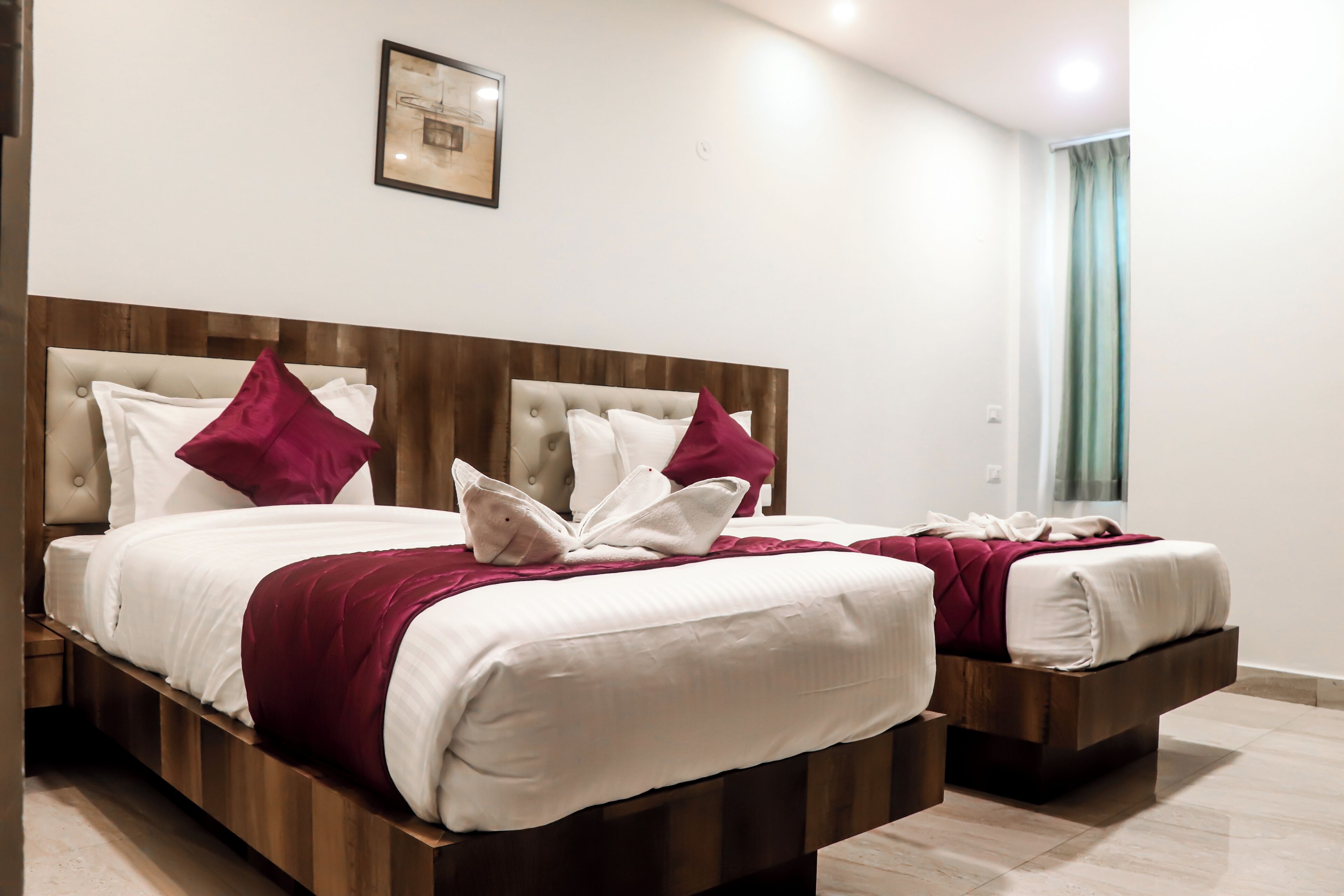 Habitación de hotel con dos camas, cada una con ropa de cama blanca y detalles rojos, cabeceros de madera y un cuadro en la pared.