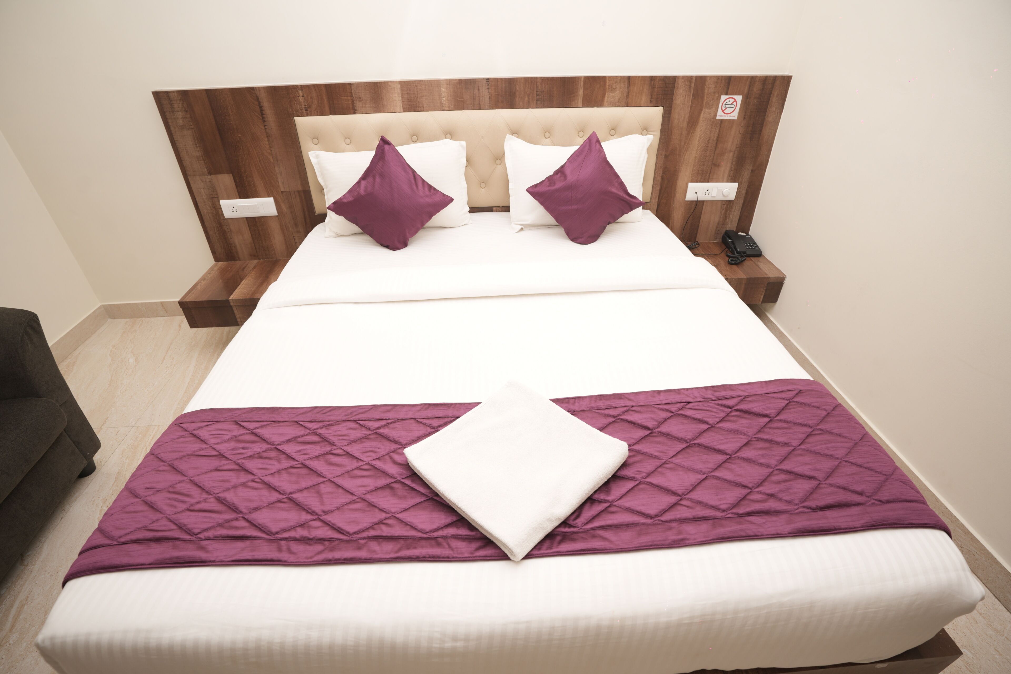 A neatly made bed with a wooden headboard, two white pillows, and a purple throw blanket.