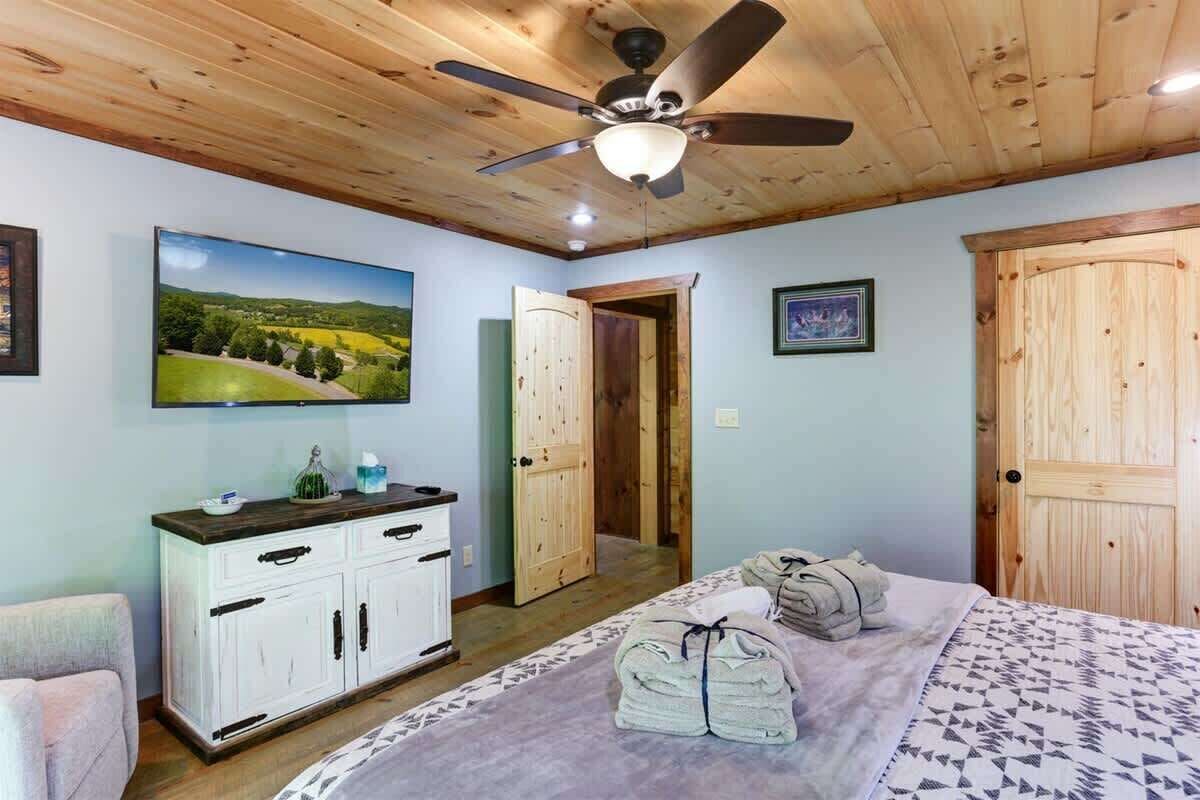 Une chambre à coucher avec un lit, un ventilateur de plafond, une armoire en bois et un tableau accroché au mur.
