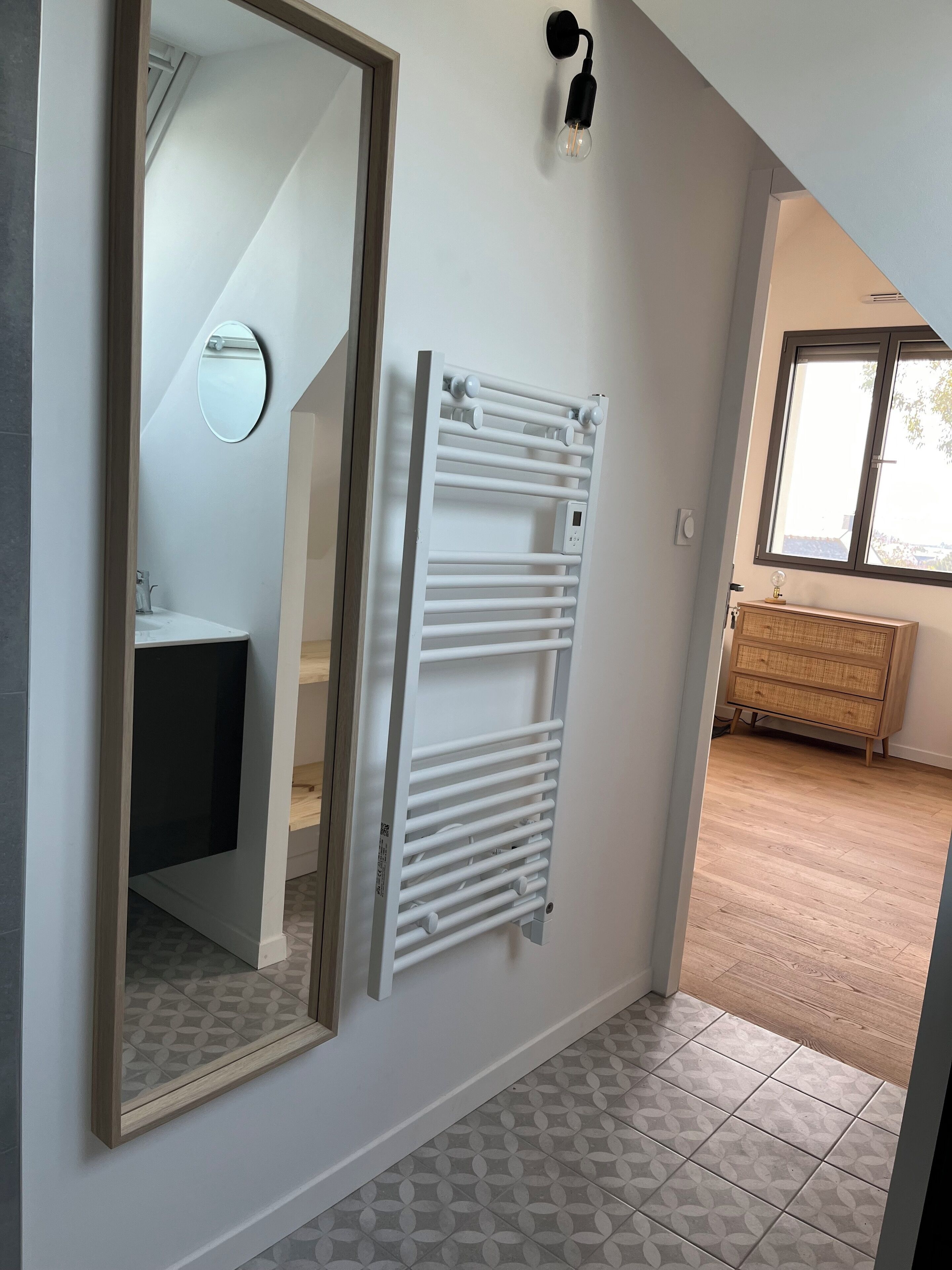 A modern bathroom with a white radiator, a mirror, and a wooden cabinet.