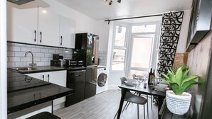 A modern kitchen with a dining area, a washing machine, and a large window with curtains. - A perfect base for exploring and relaxing, for work and leisure. Pets welcome. (Exeter)