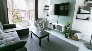 A modern living room with a grey sofa, a coffee table, a flat-screen TV mounted on the wall, and a potted plant. - A perfect base for exploring and relaxing, for work and leisure. Pets welcome. (Exeter)