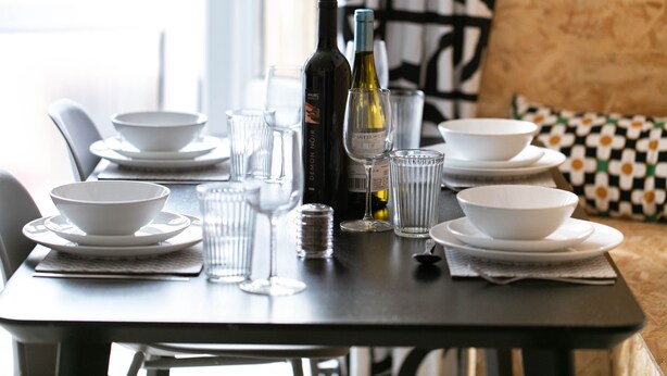 A dining table set with white bowls, plates, and glasses, a bottle of wine, and a wine glass. - A perfect base for exploring and relaxing, for work and leisure. Pets welcome. (Exeter)