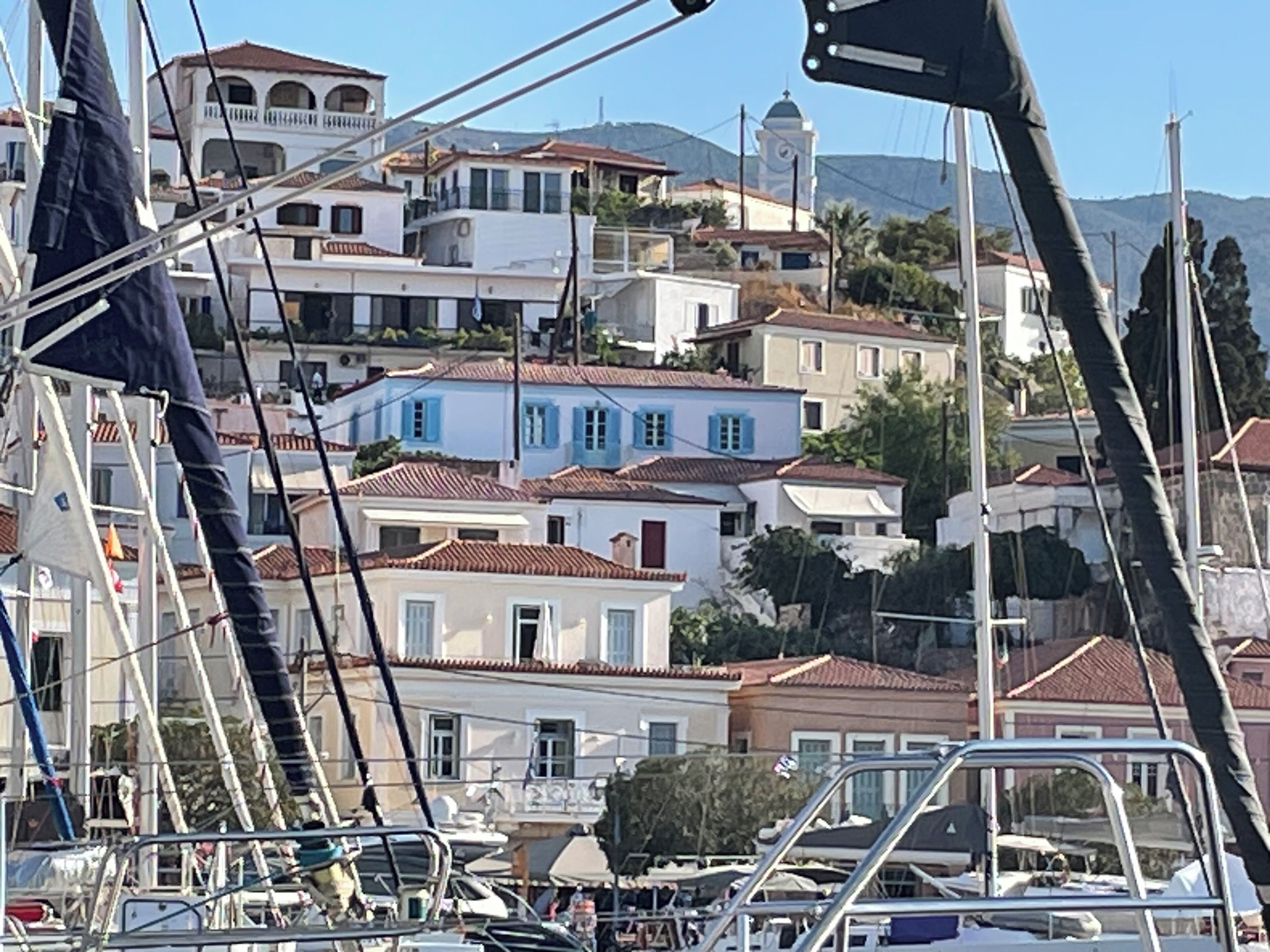 Un pueblo costero con edificios blancos y azules, una iglesia con campanario y barcos amarrados en primer plano.