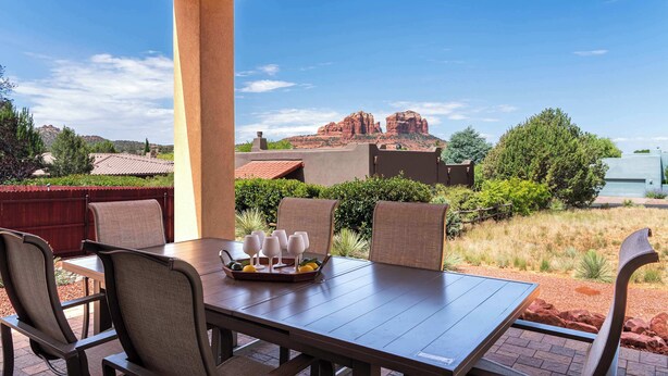 Eine Terrasse im Freien mit Tisch, Stühlen, Gläsern auf einem Tablett und Blick auf rote Felsformationen.
