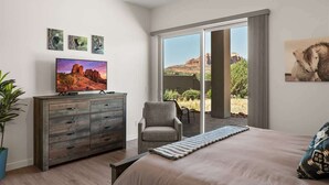 Ein Schlafzimmer mit einem Bett, einem Fernseher auf einer Kommode, einem Sessel und einer Glastür, die zu einem Außenbereich führt.