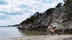 A coastal beach with rocky cliffs and calm water. - 6 Person Holiday Home in Sondeled (Risør)