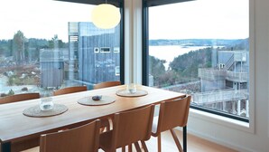 A dining area with a wooden table and chairs, large windows offering a view of buildings and a body of water. - 6 Person Holiday Home in Sondeled (Risør)