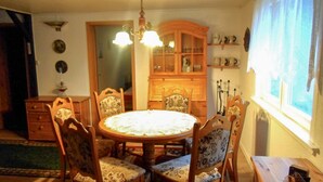 A dining area with a round table, floral upholstered chairs, a wooden cabinet, and a window with curtains. - Beautiful Querbach hut With Spring Water (Konigsee)