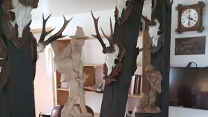 A room with a wooden sculpture of a deer and antlers, a clock, and a framed picture on the wall. - Beautiful Querbach hut With Spring Water (Konigsee)