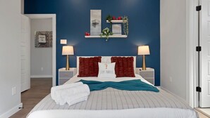 Een net opgemaakt bed met een wit en teal deken, twee bedlampen en een wandplank met decoratieve items.