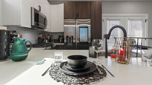 Een moderne keuken met roestvrijstalen apparatuur, een eethoek met een tafel gedekt voor twee personen, en een uitzicht op de stad door het raam.