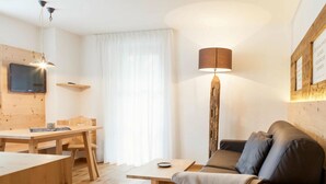 A modern living room with a wooden dining table, a sofa, and a floor lamp. - Sittnerhof Agriturismo - Apartment Goethe (Merano)