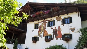 A building with a mural depicting a historical scene, a balcony with flowers, and a staircase leading to the entrance. - Sittnerhof Agriturismo - Apartment Goethe (Merano)
