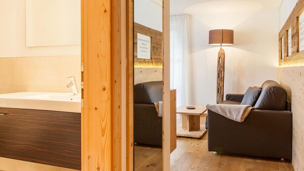 A modern room with a wooden floor, a sofa, a lamp, and a small table. - Sittnerhof Agriturismo - Apartment Goethe (Merano)
