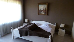 A bedroom with a white bed, two bedside tables with lamps, a painting on the wall, and a window with curtains. - Pleasant Apartment in Xanten (Xanten)