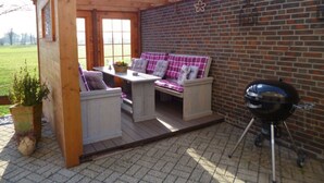 A patio area with a wooden table and two cushioned benches, a brick wall, and a barbecue grill. - Pleasant Apartment in Xanten (Xanten)