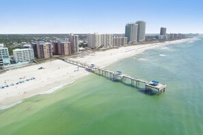 A coastal cityscape with a beach, a pier, and high-rise buildings.