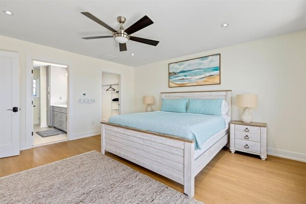 A bedroom with a bed, a ceiling fan, a nightstand, and a painting on the wall.