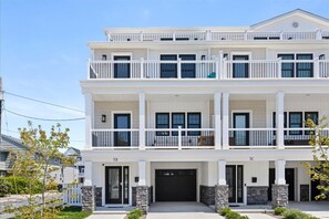 A two-story residential building with a white exterior, multiple balconies, and a garage.