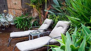 Dos sillones con cojines en una terraza de madera, rodeados de plantas verdes y una valla de bambú.