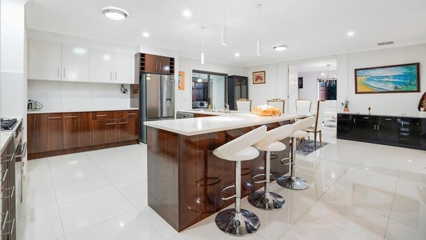 Una cocina moderna con una isla central, taburetes de bar y un comedor con una araña.