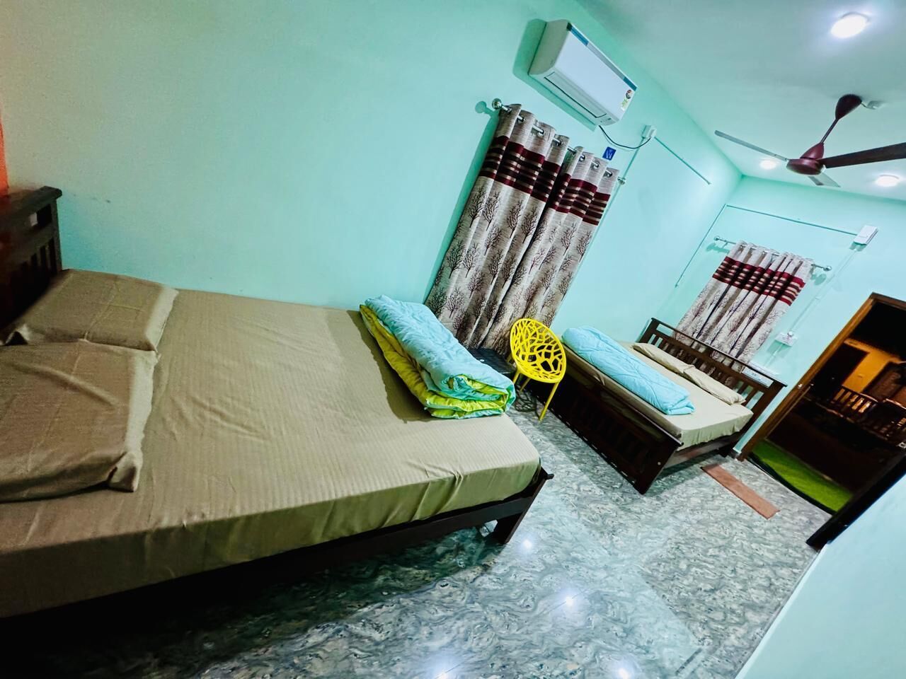 A room with two beds, a ceiling fan, an air conditioning unit, and a window with curtains.