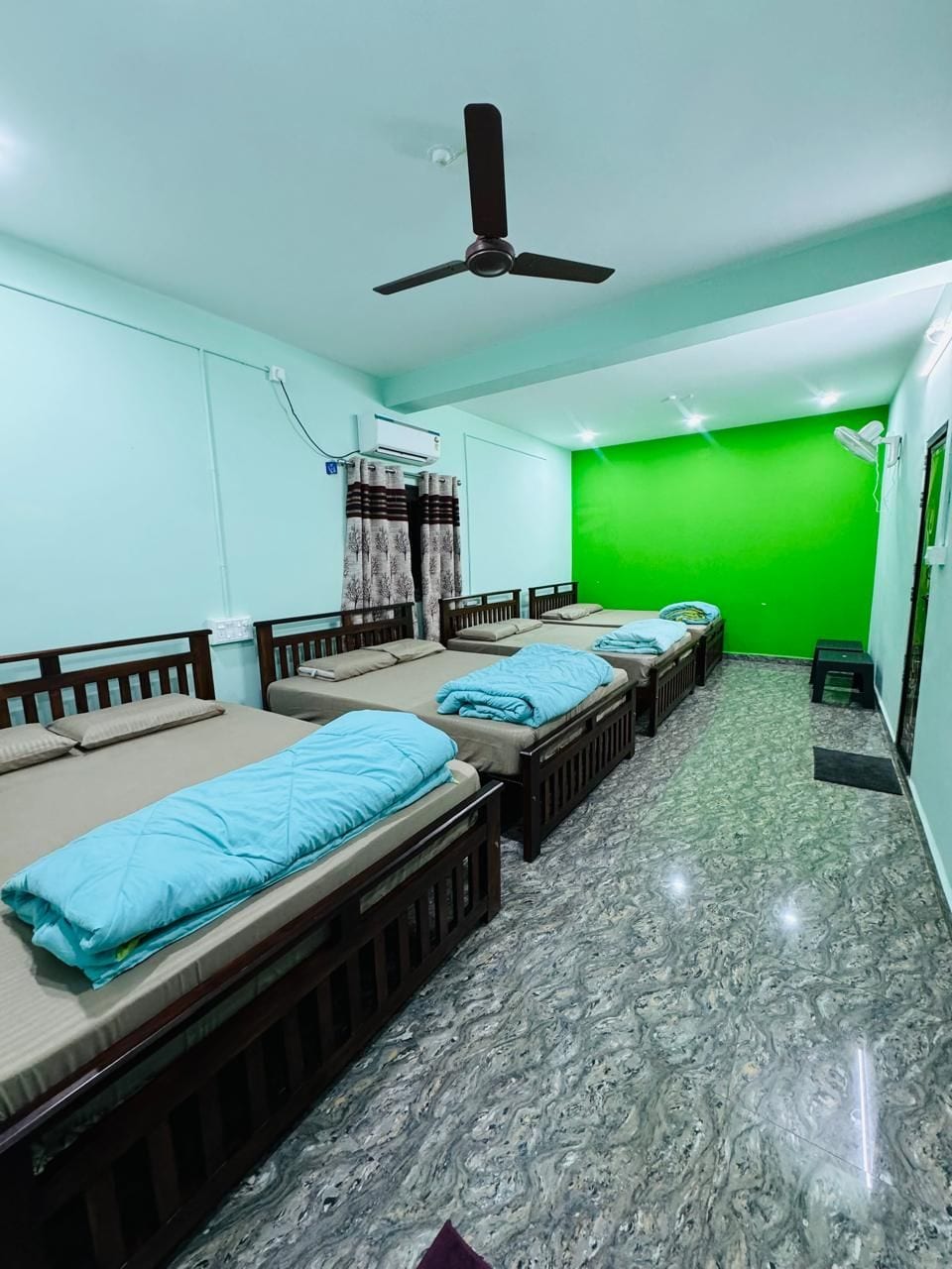 A room with four single beds, a ceiling fan, an air conditioning unit, and a green wall.