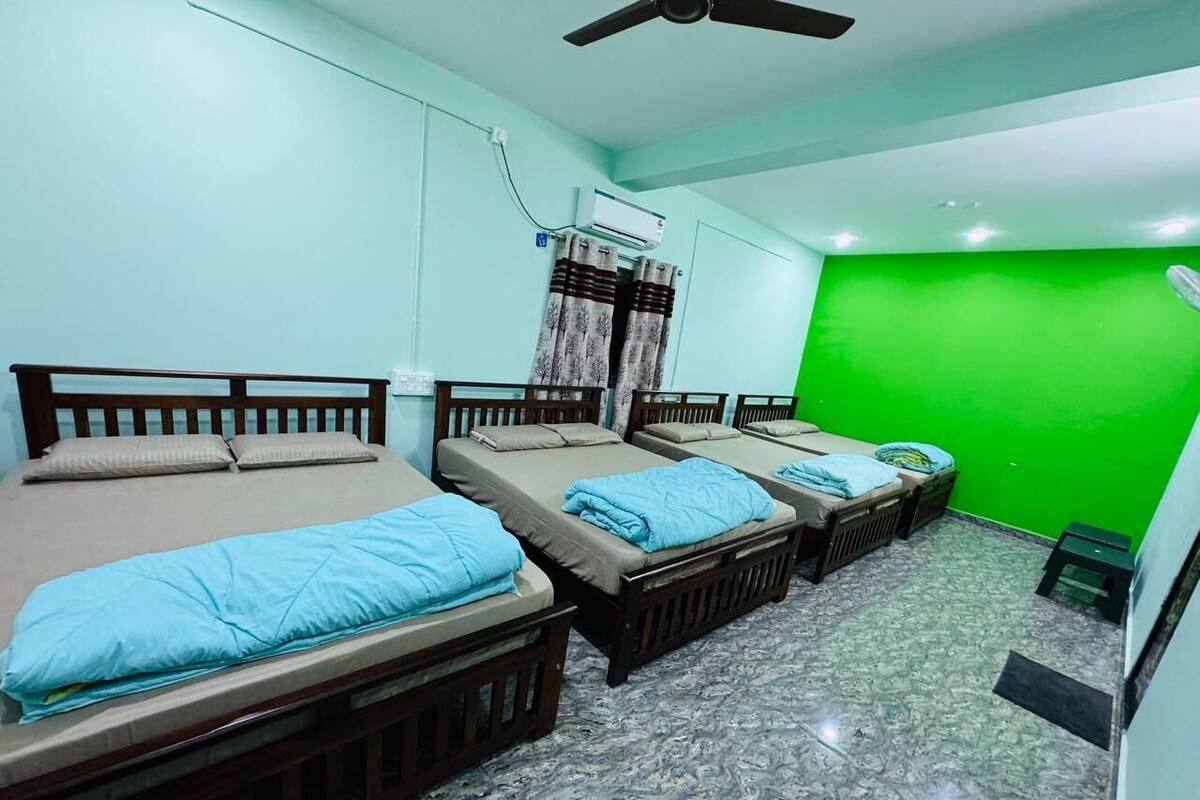 Ein Zimmer mit vier Einzelbetten, einem Deckenventilator, einer Klimaanlage und einer grünen Wand.