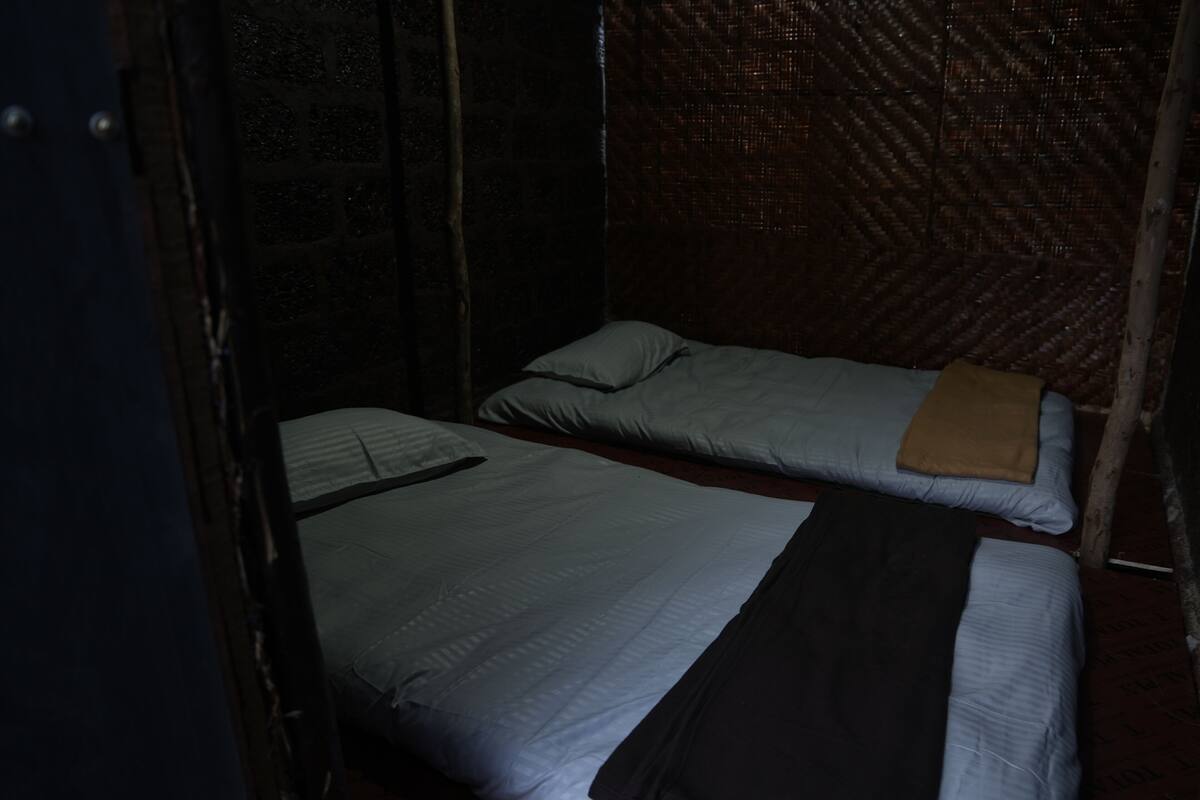 Ein kleiner, schummrig beleuchteter Raum mit zwei Einzelbetten, jeweils mit Kissen und Decke.