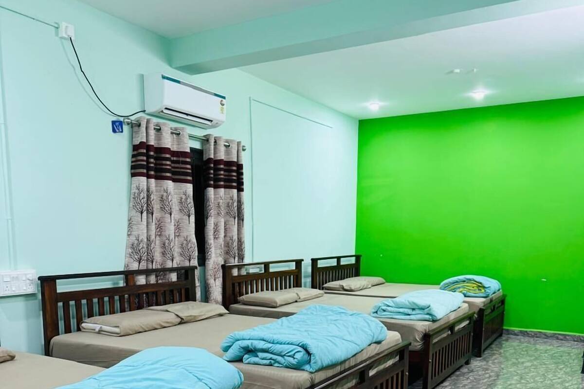 Ein Zimmer mit vier Einzelbetten, einem Deckenventilator, einer Klimaanlage und einer grünen Wand.