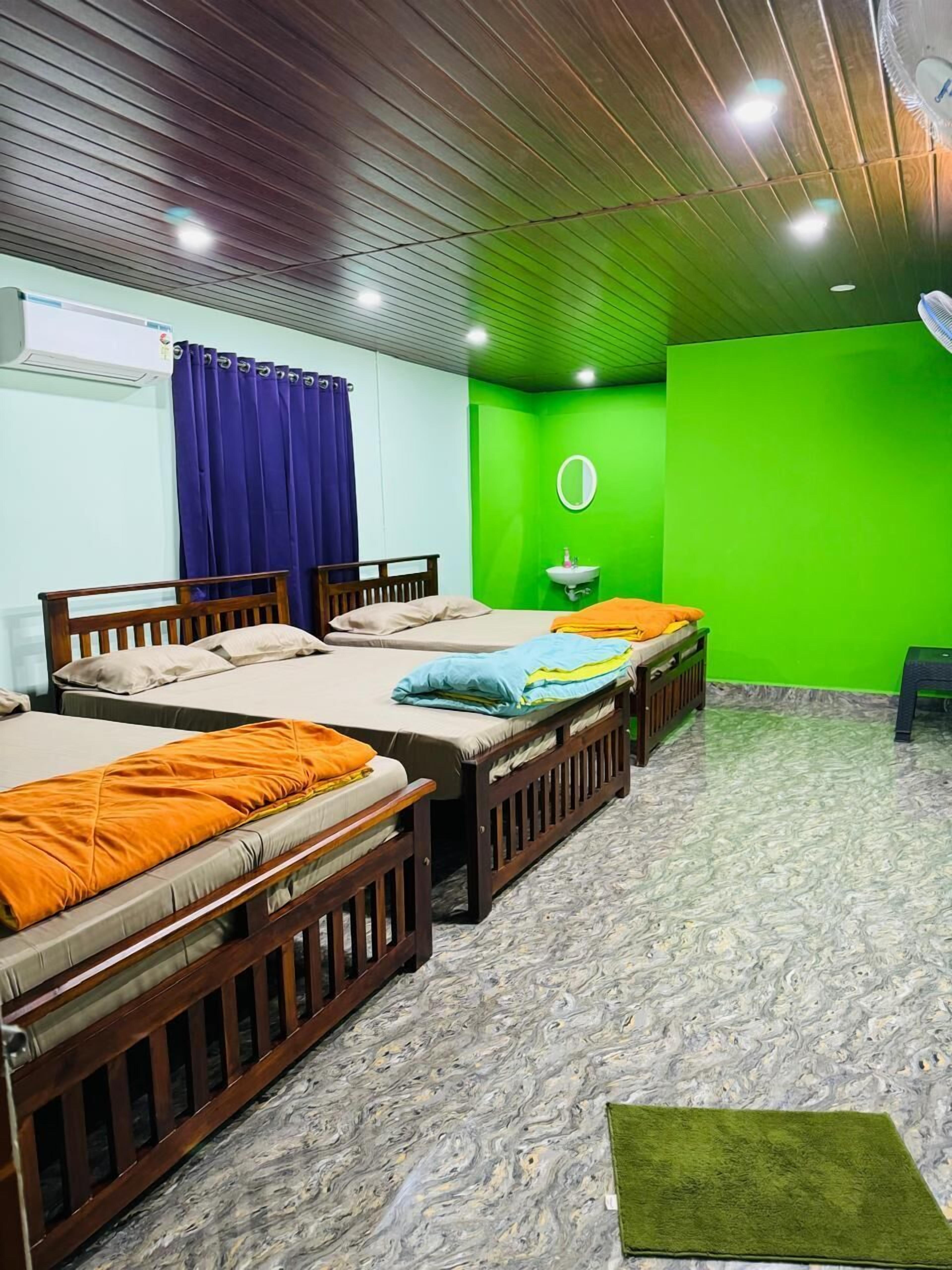 A room with three wooden beds, a blue curtain, a green wall, a round mirror, and a small sink.