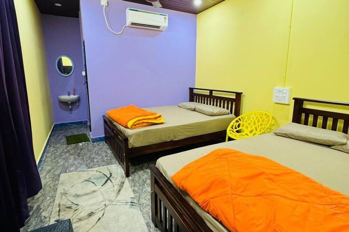 Ein Zimmer mit zwei Betten, einem kleinen Waschbecken und einem Deckenventilator.