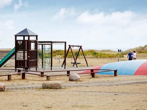 Une aire de jeux avec une structure d’escalade, des balançoires et un toboggan.