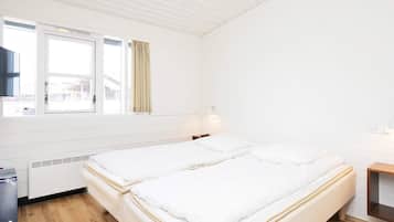 Habitación de hotel con dos camas, una ventana con cortinas, una mesita de noche y una lámpara fijada a la pared.