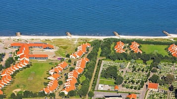 Vista aérea de una zona residencial costera con filas de casas, una playa y un edificio grande con tejado rojo.