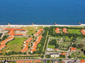 An aerial view of a coastal residential area with rows of houses, a beach, and a large building with a red roof.