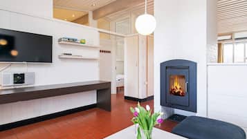 Una sala de estar moderna con chimenea, un televisor de pantalla plana y un jarrón de flores sobre una mesa.