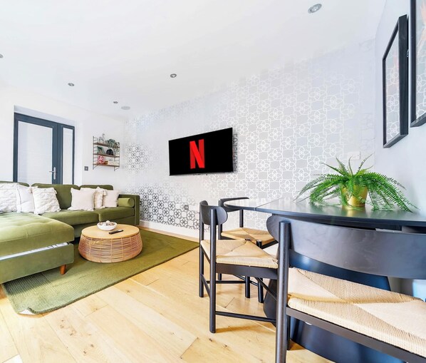 A modern living room with a green sofa, a round coffee table, and a TV mounted on the wall displaying the Netflix logo.