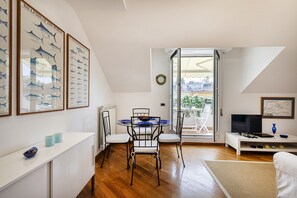 A dining area with a round table, chairs, and a white cabinet. There are framed pictures on the wall and a TV on a white stand. - The Fisherman s House by Wonderful Italy (Rapallo)
