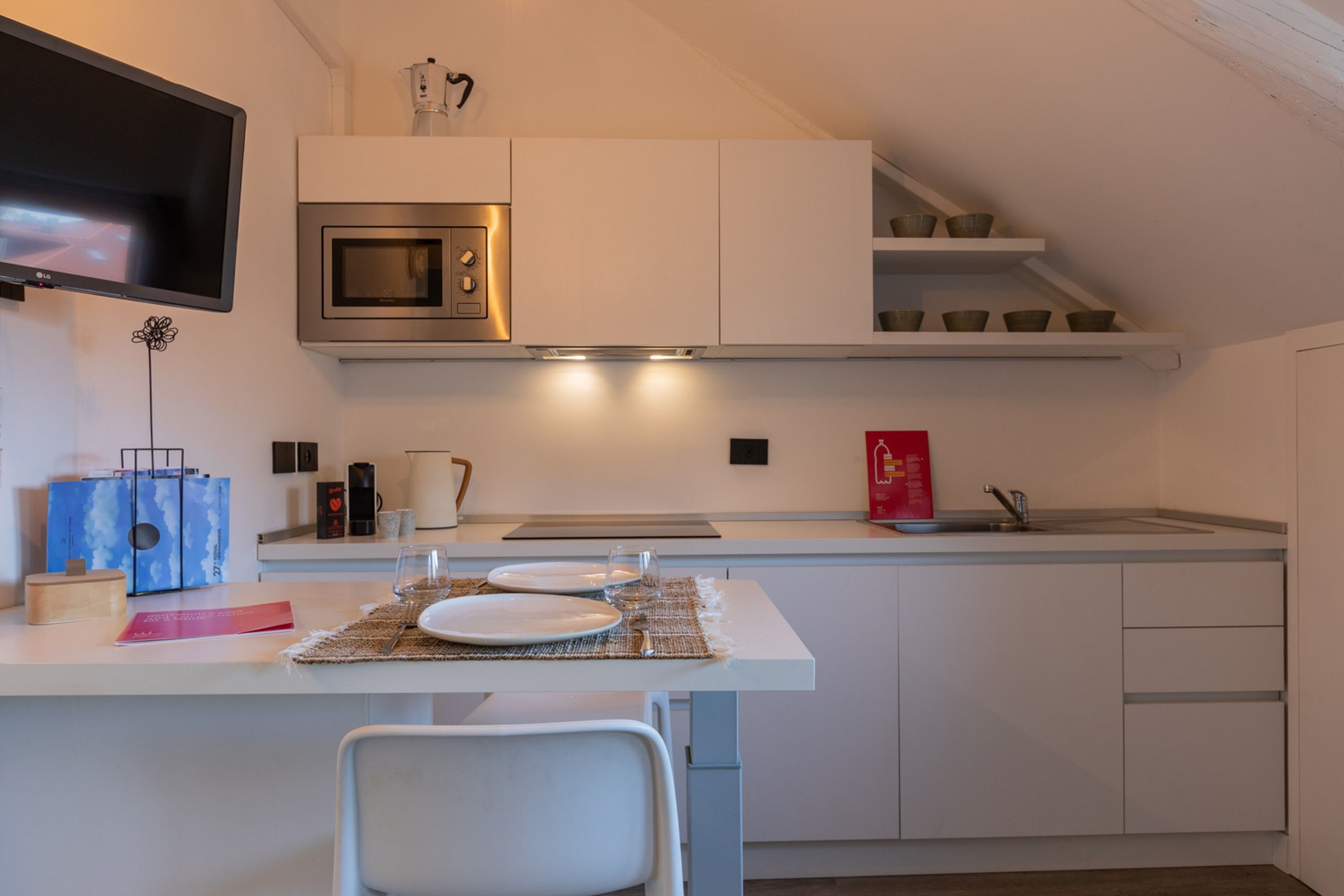 A modern kitchen with white cabinetry, a built-in microwave, and a small dining area with a table set for two.