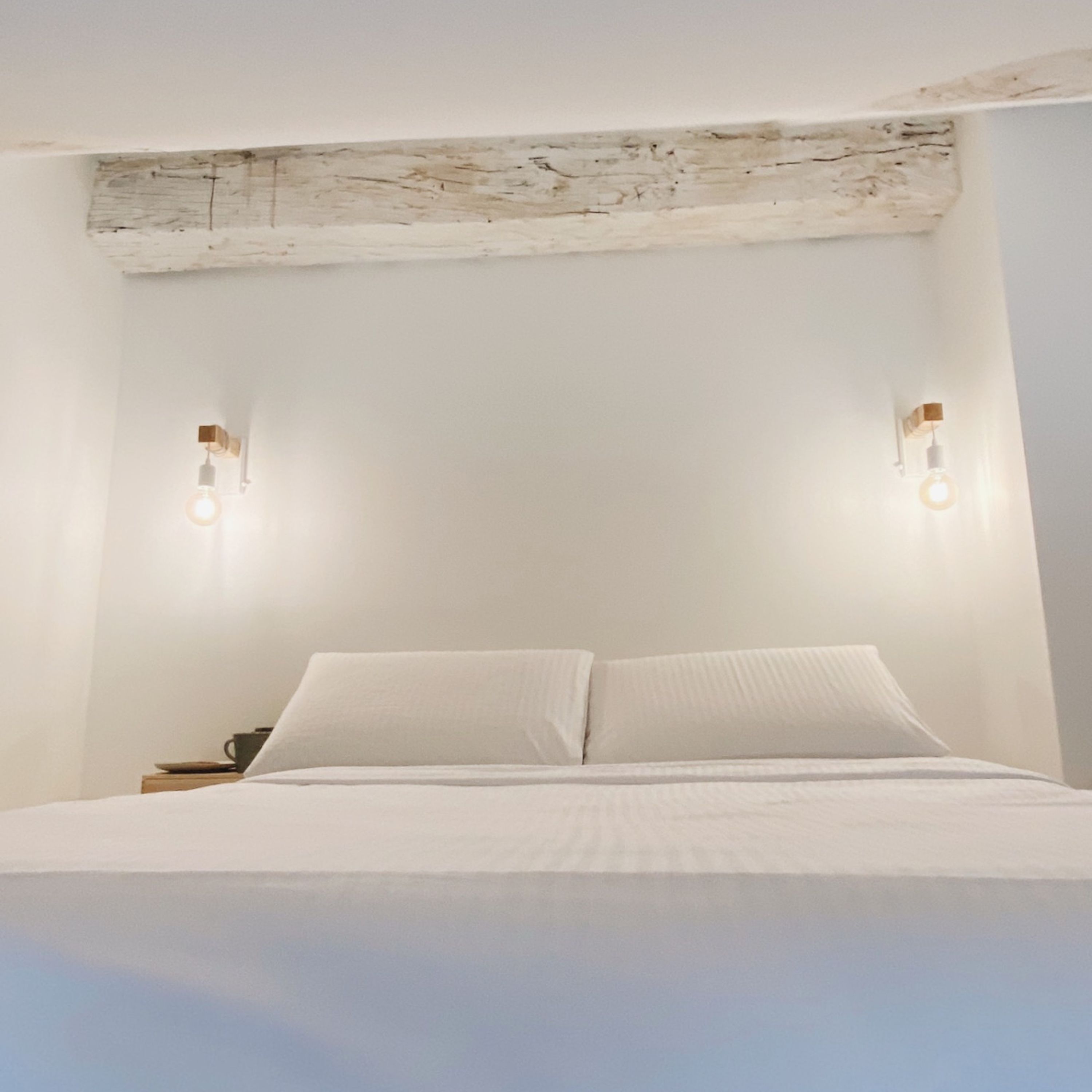 Un letto con biancheria bianca, due lampade a parete e un soffitto rustico.