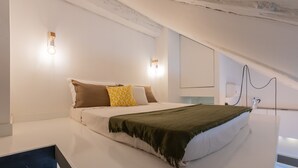 Ett modernt sovrum med en stor säng, vita väggar och ett sluttande tak.