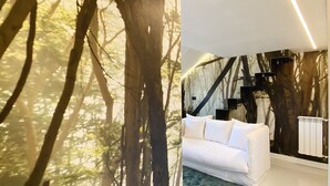 En modern inredning med en vit soffa, en mönstrad matta och en vägg dekorerad med en väggmålning som föreställer ett träd.