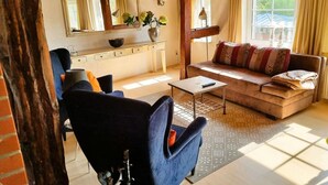 Sala de estar aconchegante com sofá, poltrona, mesa de centro e área de cozinha com janela.