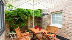 Um pátio com mesa e cadeiras, um guarda-sol branco e um muro de tijolos com plantas.