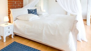 Quarto com cama de dossel, roupa de cama branca, mesa de cabeceira com abajur e tapete azul.